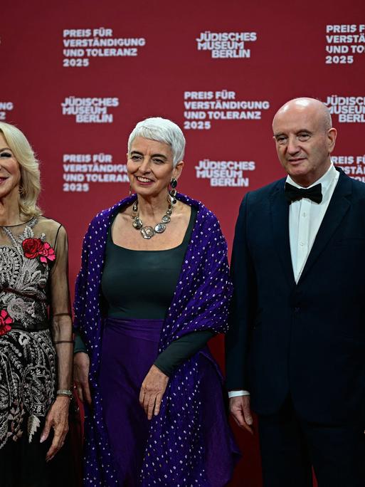 Die Direktorin des Jüdischen Museums Berlin, Hetty Berg (m.), mit den Preisträgern Amy Gutmann (l.) und Daniel Zajfman (r.); sie stehen in Abendgarderobe nebeneinander auf einer Bühne. 