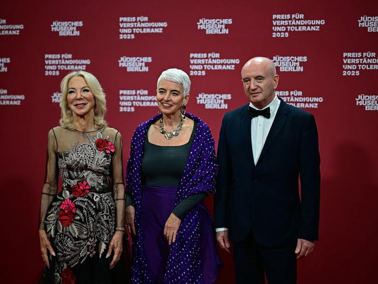 Die Direktorin des Jüdischen Museums Berlin, Hetty Berg (m.), mit den Preisträgern Amy Gutmann (l.) und Daniel Zajfman (r.); sie stehen in Abendgarderobe nebeneinander auf einer Bühne. 