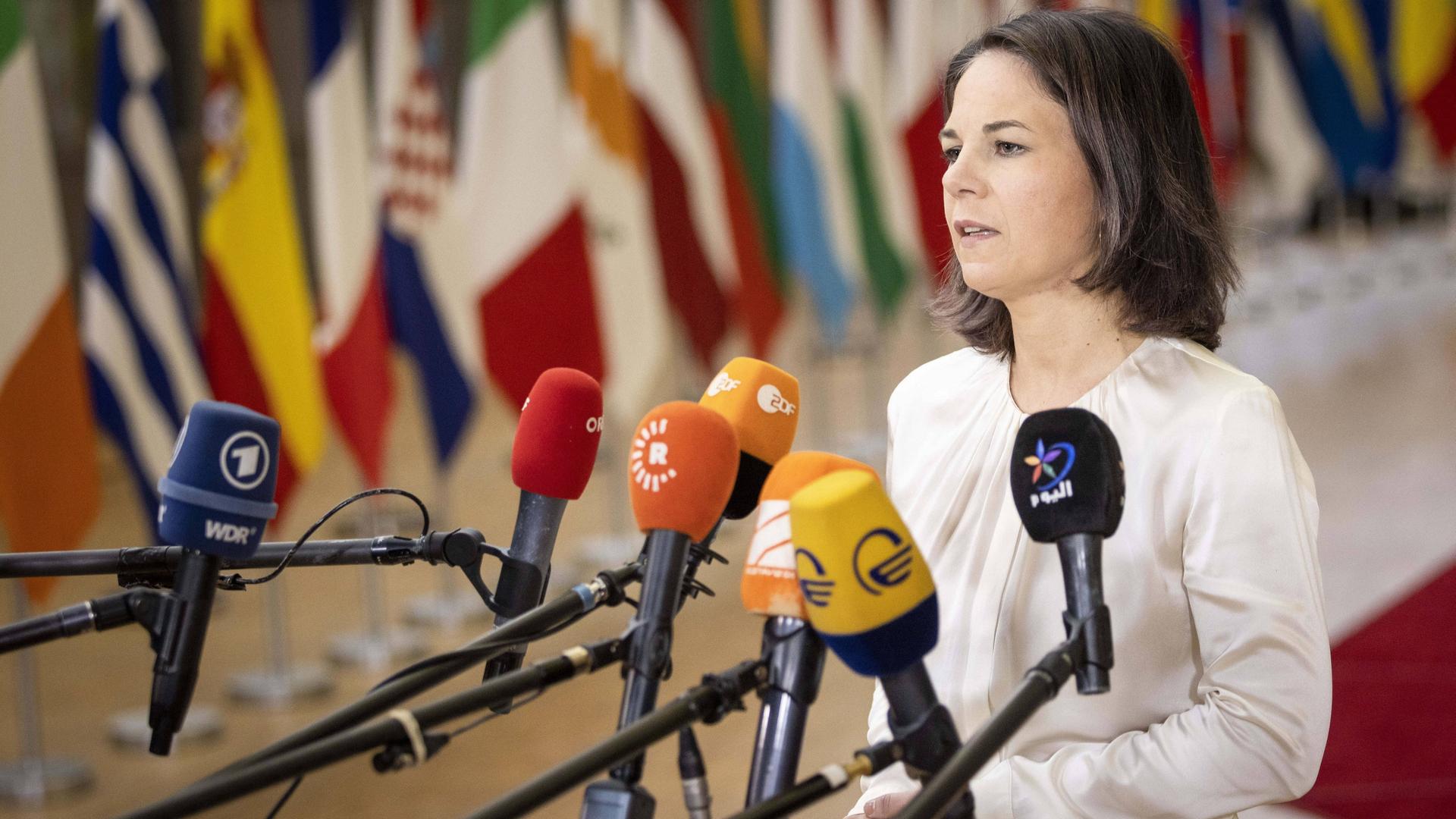 Bundesaußenministerin Baerbock steht in Brüssel vor Mikrofonen und gibt ein Statement. Im Hintergrund verschwommen die Fahnen der Mitgliedsländer.