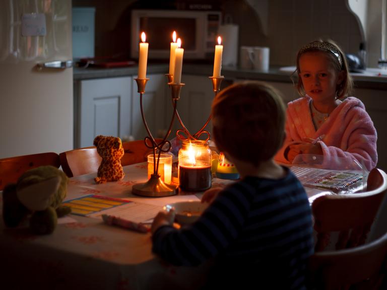 Zwei Kinder, ein Junge und ein Mädchen sitzen bei Kerzenlicht an einem Tisch