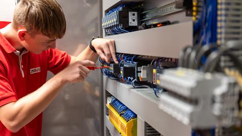 Ein Auszubildender zum Mechatroniker verdrahtet einen Schaltschrank.