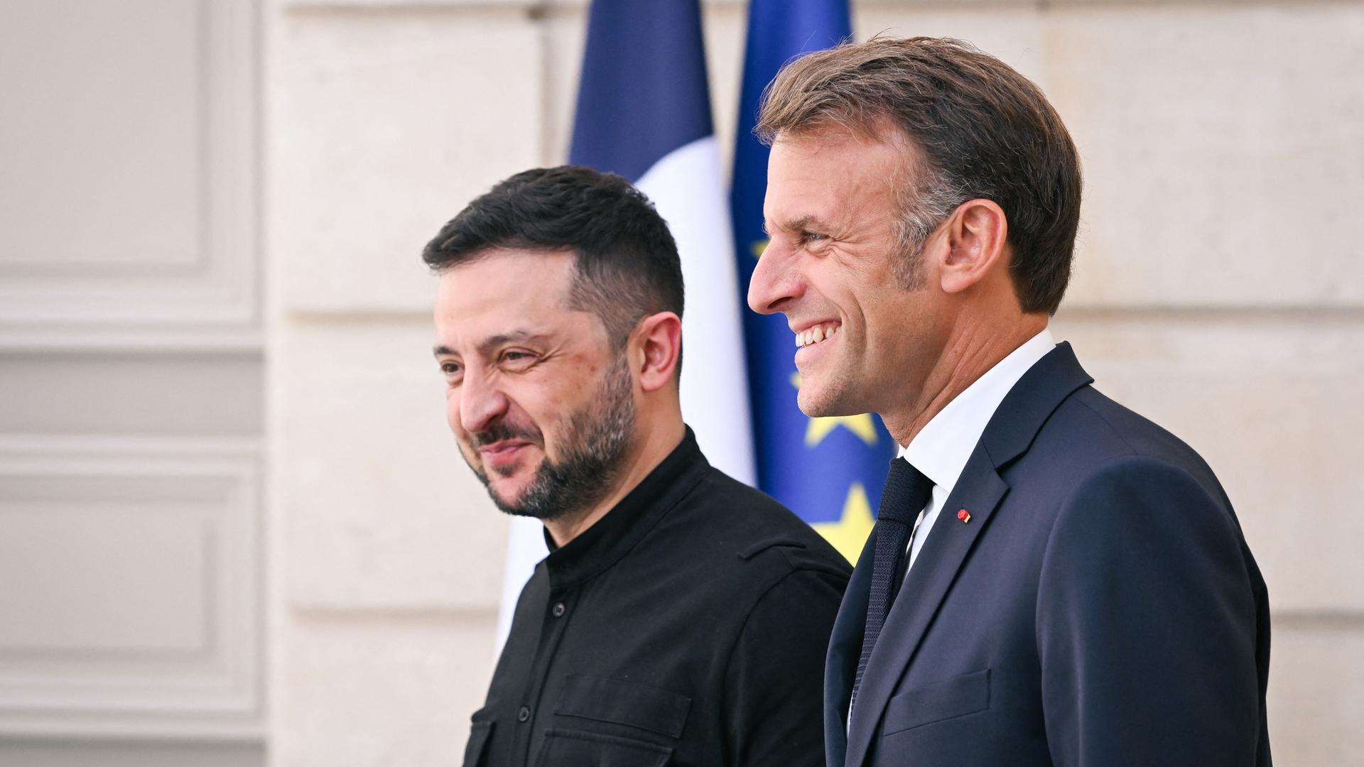 Der ukrainische Präsident Selenskyj (links) neben Frankreichs Staatschef Macron vor der ukrainischen und der Europa-Flagge. Beide lachen