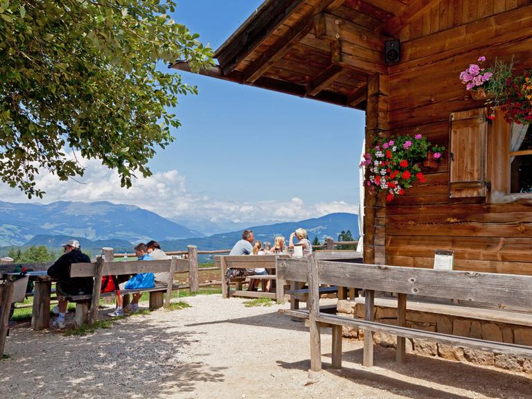 Touristen geniessen den Ausblick von der Tvon einer Almhütte in Südtirol. 