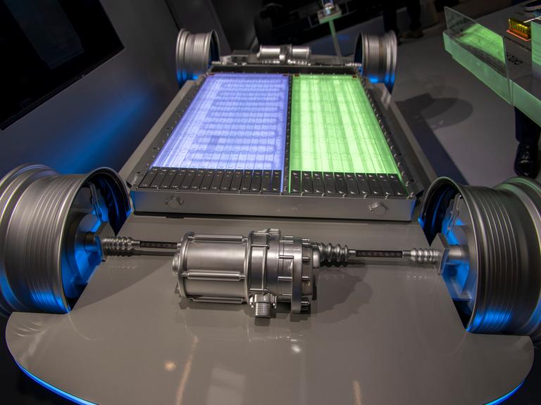 Zu sehen ist der Unterboden eines Elektrofahrzeugs ohne Karosserie, so dass die Batterie frei sichtbar ist. In der Mitte liegt ein großes, rechteckiges Batteriepaket, das aus zwei unterschiedlich farbigen Bereichen besteht. Zu sehen ist der Unterboden eines Elektrofahrzeugs ohne Karosserie, so dass die Batterie frei sichtbar ist. In der Mitte liegt ein großes, rechteckiges Batteriepaket, das aus zwei unterschiedlich farbigen Bereichen besteht.