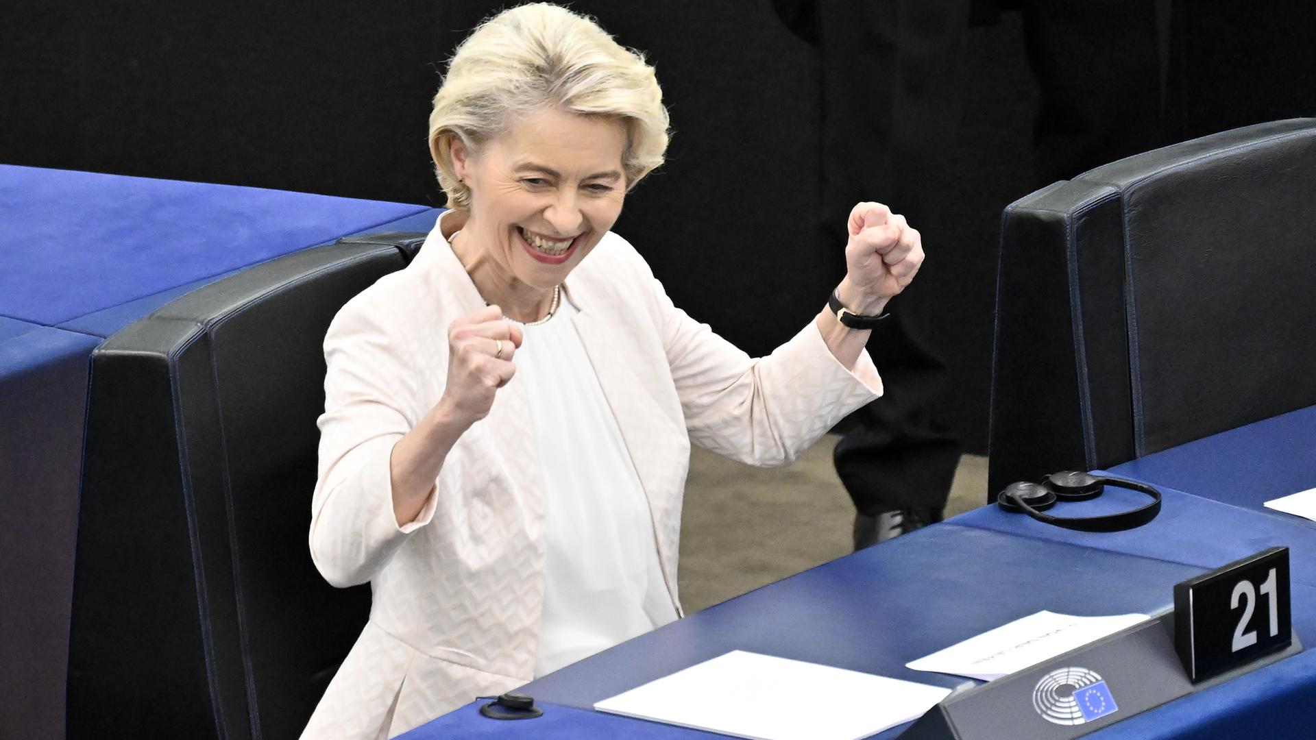 Ursula von der Leyen sitzt im Europäischen Parlament, schmeißt die Hände in die Luft und grinst.