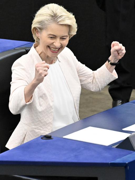 Ursula von der Leyen sitzt im Europäischen Parlament, schmeißt die Hände in die Luft und grinst.