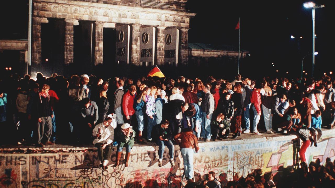 Jubelnde Menschen auf der Berliner Mauer am Brandenburger Tor. Am Abend des 09.11.1989 teilte SED-Politbüro Mitglied Günter Schabowski mit, dass alle DDR-Grenzen in die Bundesrepublik und nach West-Berlin für DDR-Bürger geöffnet werden.