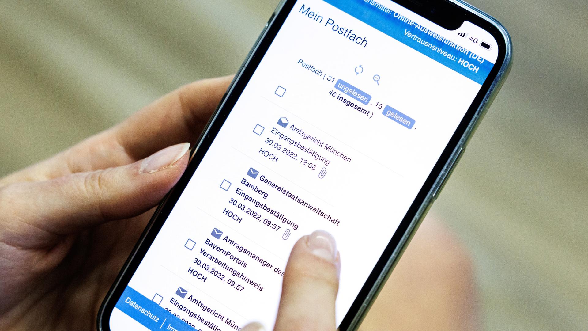 Eine Frau demonstriert bei einem Pressetermin zur Vorstellung von einem neuen Online-Zugang zum Einreichen von Klagen bei Gerichten das Prozedere zum Einreichen einer Klage über ihr Smartphone mittels der „BayernApp“.