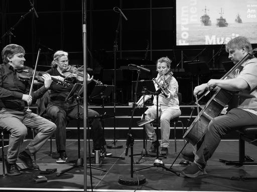 Das Asasello Quartett sitzt auf einer Bühne mit etlichen Mikrofonen und spielt konzentriert. Das Asasello Quartett sitzt auf einer Bühne mit etlichen Mikrofonen und spielt konzentriert.