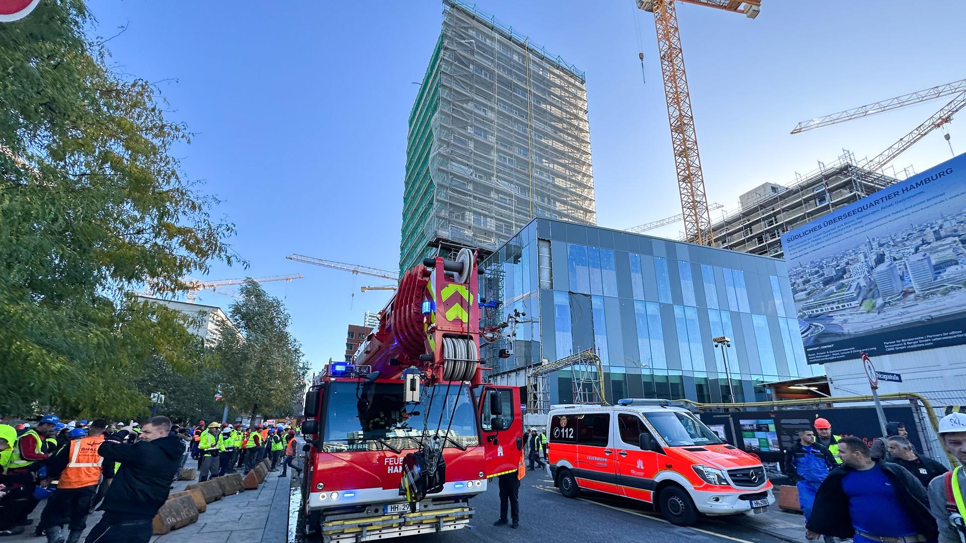 Hamburg: Einsatzfahrzeuge der Feuerwehr stehen vor einem eingerüsteten Hochhaus. Hamburg: Einsatzfahrzeuge der Feuerwehr stehen vor einem eingerüsteten Hochhaus.