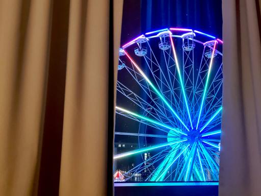 Durch ein Fenster ist ein erleuchtetes Riesenrad zu sehen. Durch ein Fenster ist ein erleuchtetes Riesenrad zu sehen.
