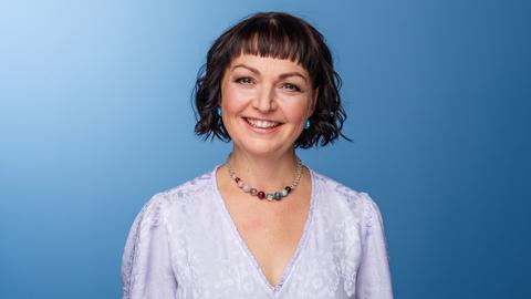 Doreen Bergmann lächelt in die Kamera. Sie trägt ein lavendelfarbenes Kleid und das dunkle Haar zu einem lockigen Bob geschnitten.