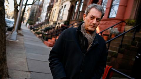 Paul Auster vor seinem Haus in Brooklyn. Er trägt eine schwarze Jacke und Schal.