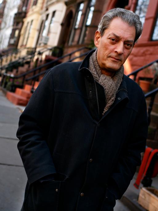 Paul Auster vor seinem Haus in Brooklyn. Er trägt eine schwarze Jacke und Schal.