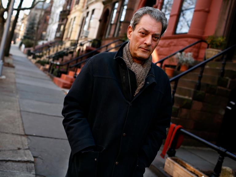 Paul Auster vor seinem Haus in Brooklyn. Er trägt eine schwarze Jacke und Schal.