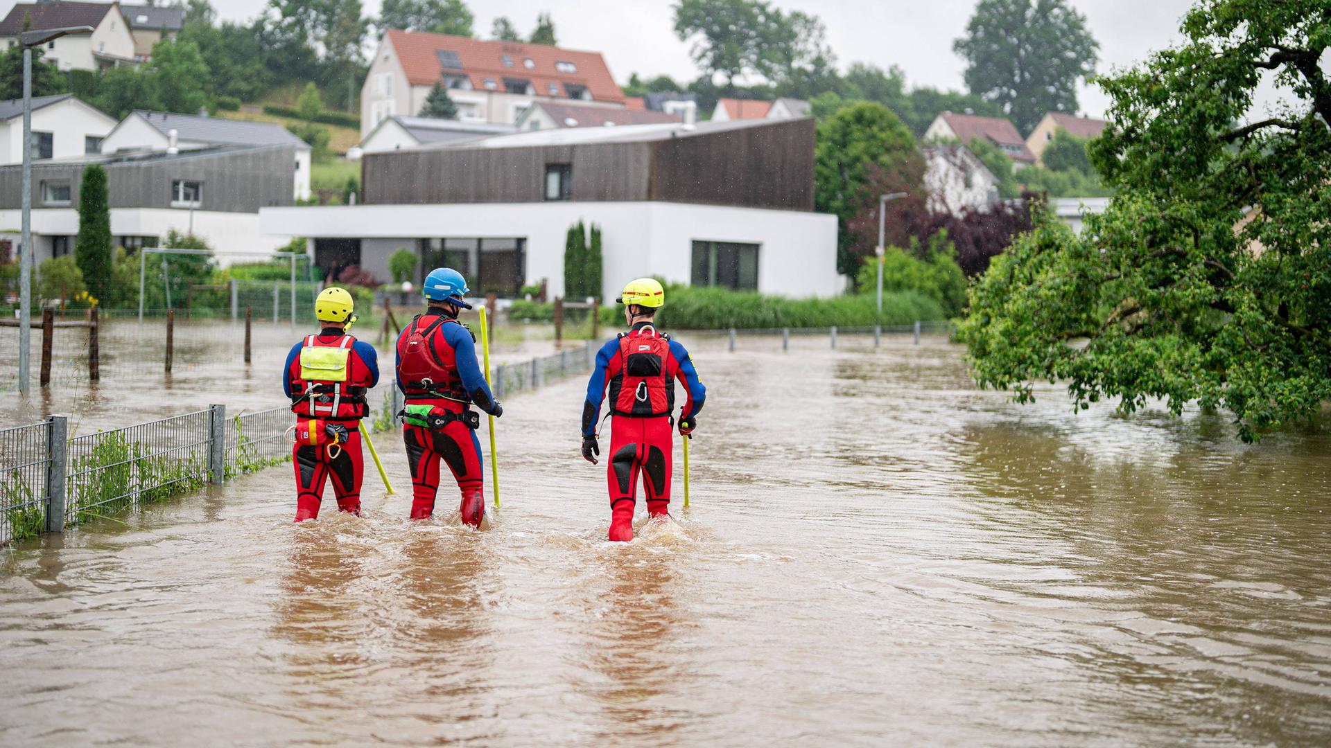 Drei Rettungskräfte der DLRG in Neu-Ulm, Bayern, laufen durch das Hochwasser in einem Wohngebiet.
      