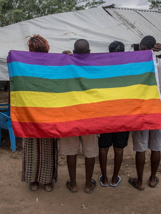 Flüchtlinge aus Uganda in einem Flüchtlingscamp im Nordwesten von Kenia. Sie halten eine auf den Kopf gedrehte Regenbogenflagge in den Händen.
