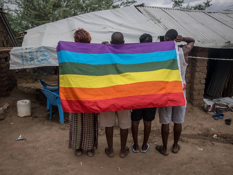 Flüchtlinge aus Uganda in einem Flüchtlingscamp im Nordwesten von Kenia. Sie halten eine auf den Kopf gedrehte Regenbogenflagge in den Händen.
