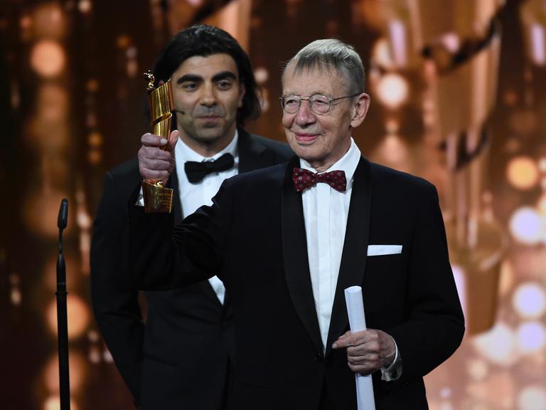 Der Filmemacher Hark Bohm streckt auf einer Veranstaltung in 2018 einen Preis in die Höhe - hinter ihm steht der Regisseur Fatih Akin.