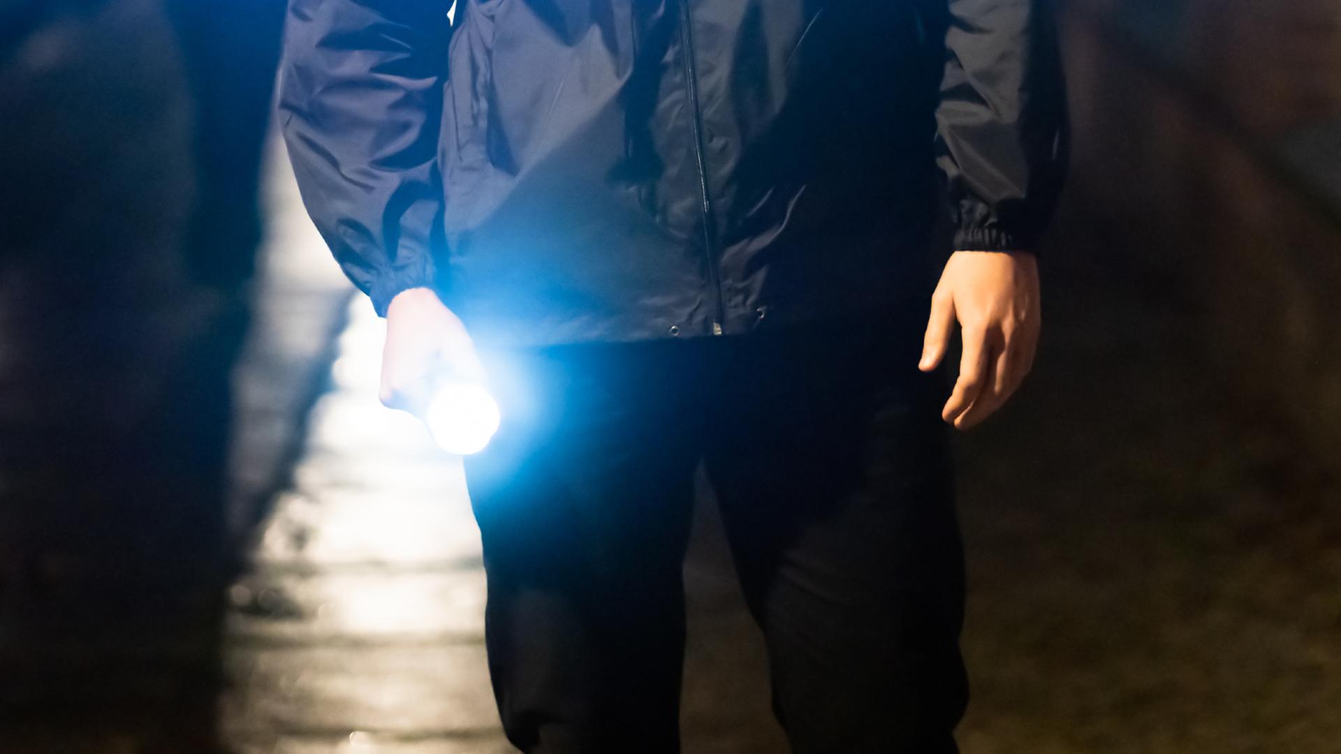 Ein Mann leuchtet nachts mit einer Taschenlampe auf einen Gehweg.