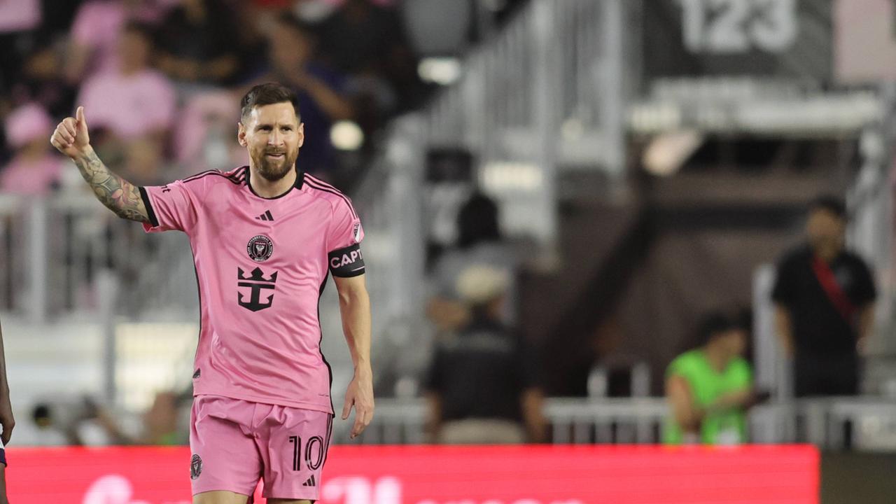 Messi im rosa Trikot steht mit "Daumen hoch"-Geste auf dem Spielfeld, dahinter unscharf eine Tribüne.