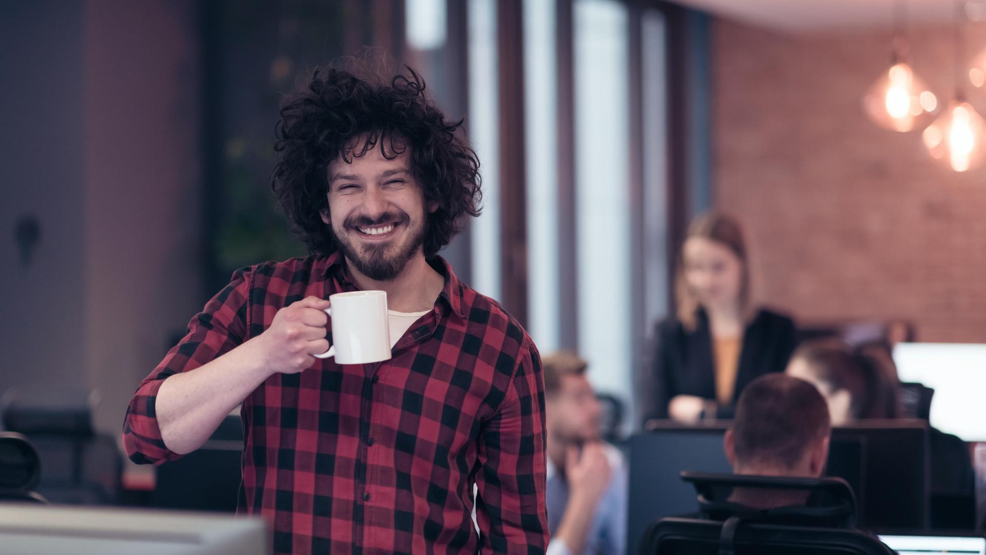 Junger Mann mit Kaffeetasse im Büro, lächelnd