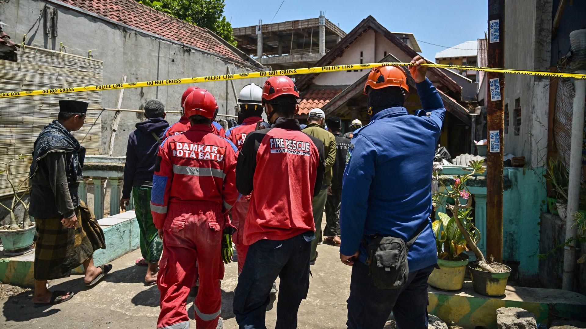 Indonesische Rettungskräfte verlassen den Einsturzort, man sieht sie von hinten.