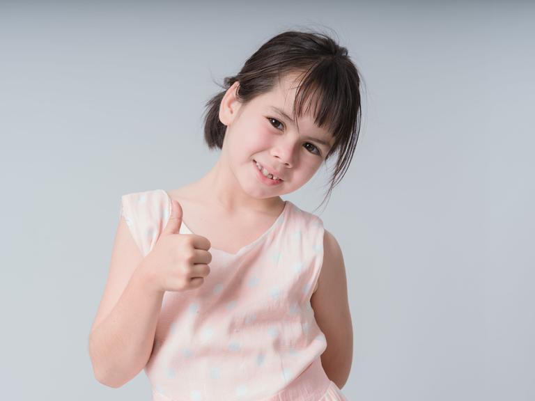 Ein Mädchen schaut zustimmend in die Kamera, sie hat den Daumen hoch gehalten und lächselt