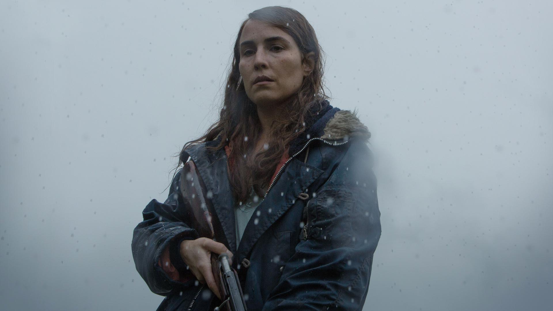 Hauptdarstellerin Noomi Rapace als Schafzüchterin Maria mit einem Gewehr in der Hand. Im Hintergrund wabert Nebel.