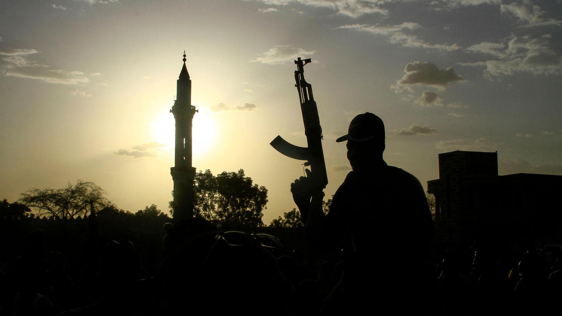 Vor einem Sonnenuntergang hebt sich die Silhouette eines Minaretts und eines Kämpfers mit erhobener Waffe ab.