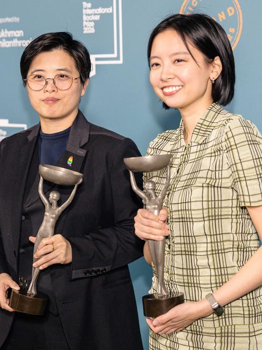 Zwei Frauen stehen nebeneinander und lächeln. Sie halten jeweils eine Statuette in silber.