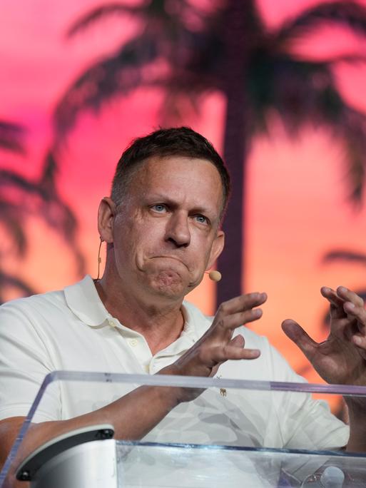 Peter Thiel steht an einem Redepult und gestikuliert mit den Händen. 