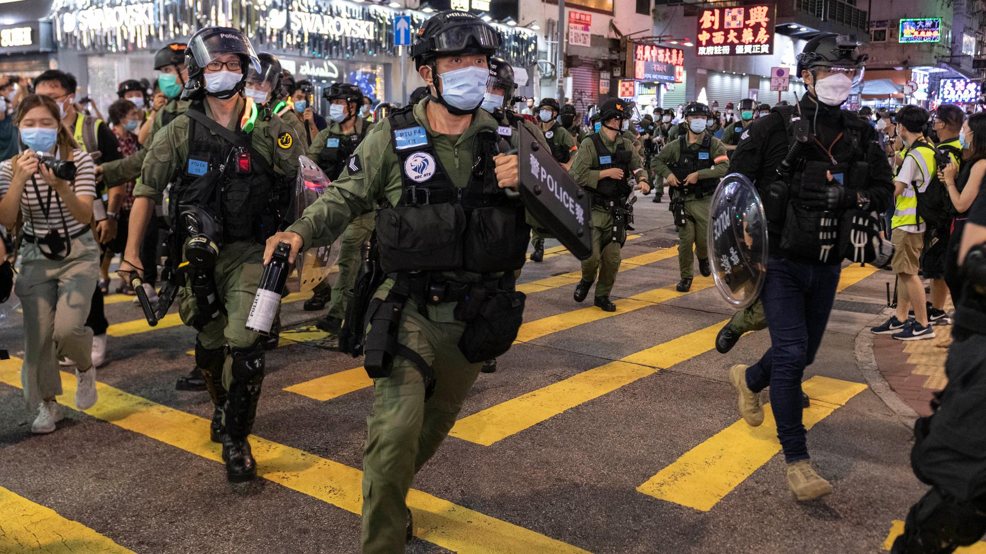 Bewaffnete Sicherheitskräfte mit Mundschutz laufen äußerlich angespannt über eine Straße in Hongkong Bewaffnete Sicherheitskräfte mit Mundschutz laufen äußerlich angespannt über eine Straße in Hongkong