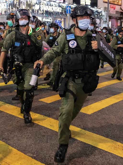 Bewaffnete Sicherheitskräfte mit Mundschutz laufen äußerlich angespannt über eine Straße in Hongkong