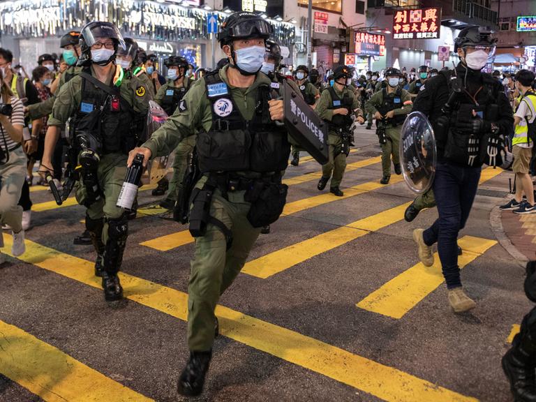Bewaffnete Sicherheitskräfte mit Mundschutz laufen äußerlich angespannt über eine Straße in Hongkong