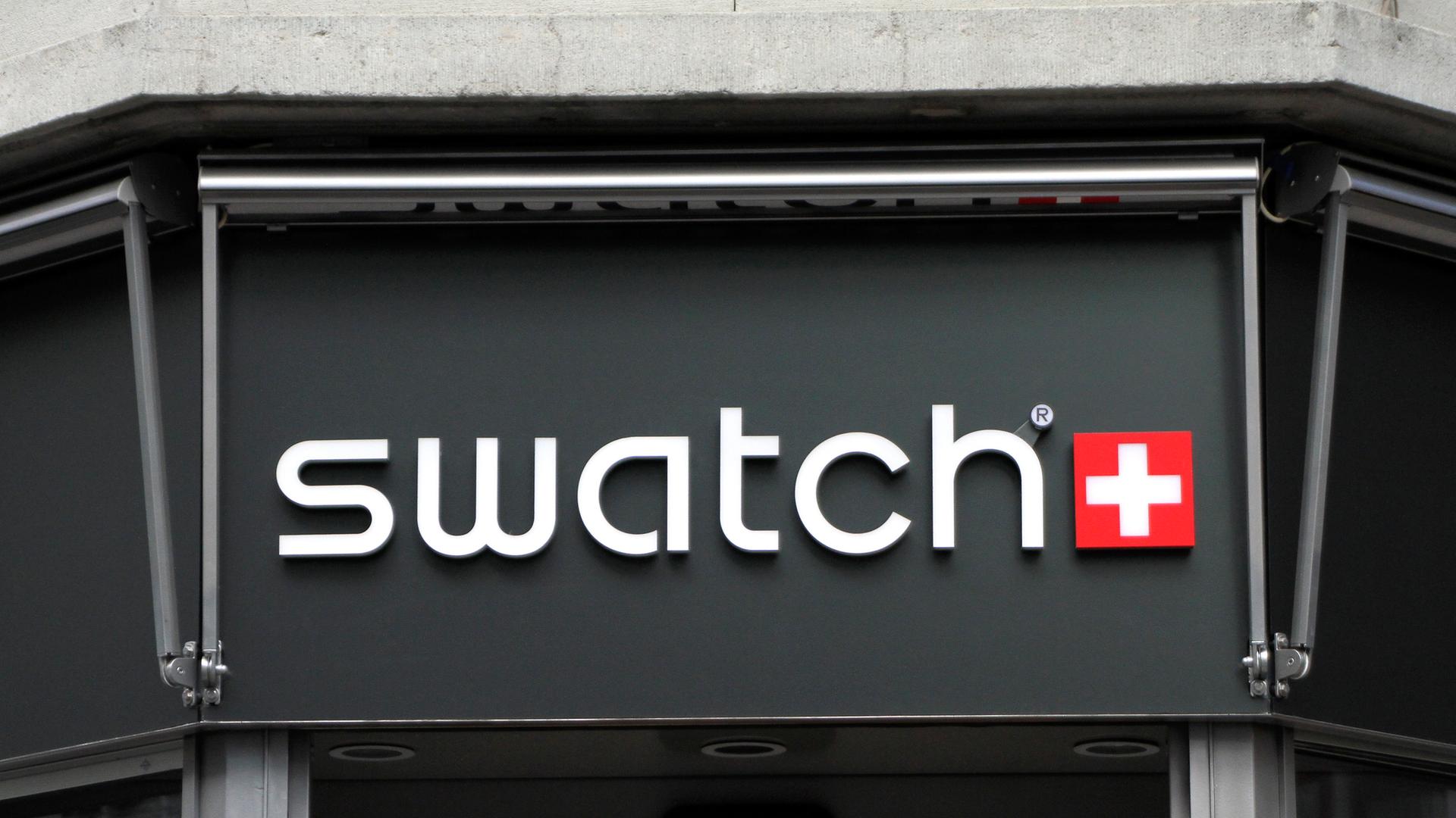 In weißen Leuchtbuchstaben steht SWATCH auf schwarzem Hintergrund. Rechts daneben ist das Wappen der Schweiz zu sehen. Ein weißes Kreuz auf rotem Grund. In weißen Leuchtbuchstaben steht SWATCH auf schwarzem Hintergrund. Rechts daneben ist das Wappen der Schweiz zu sehen. Ein weißes Kreuz auf rotem Grund.
