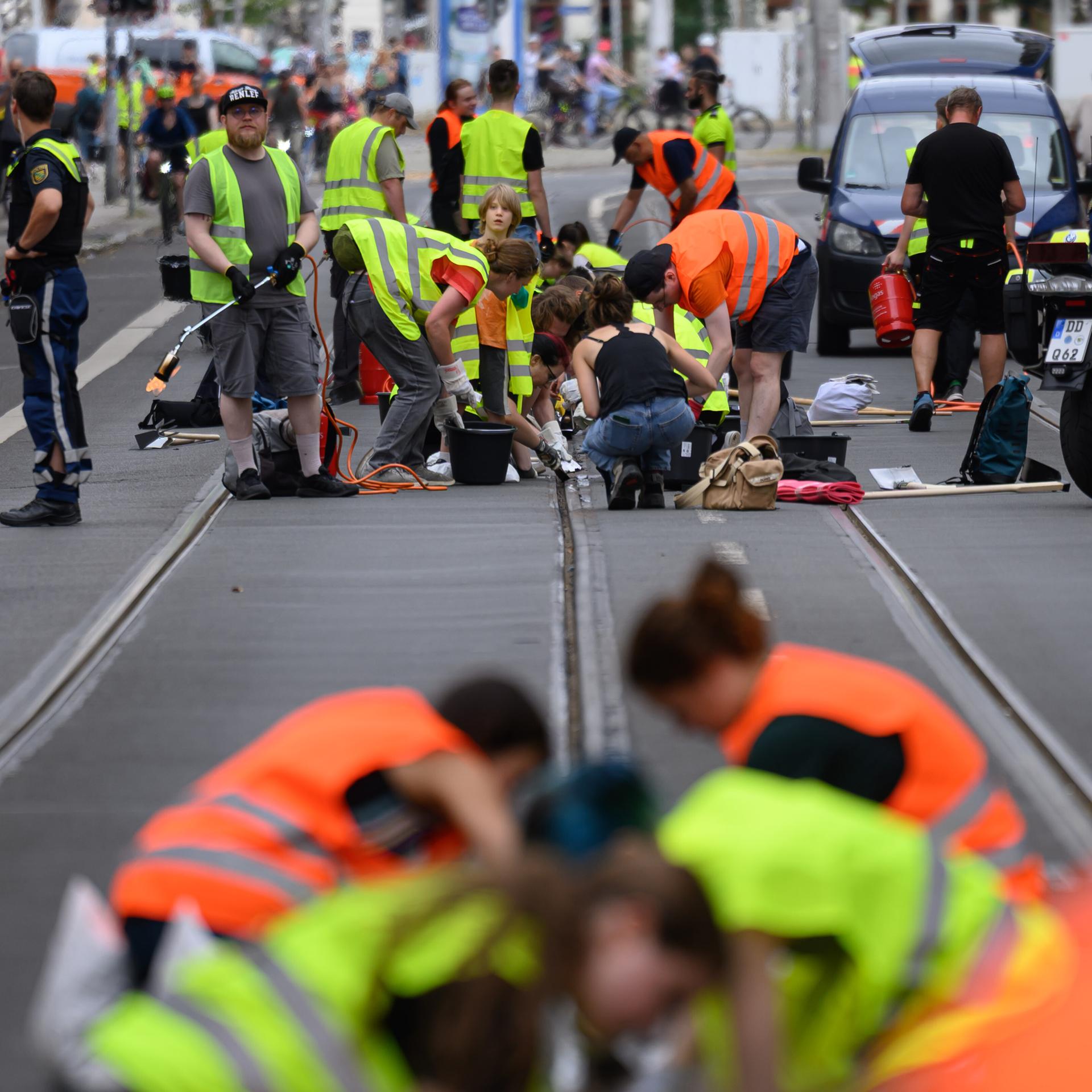 Freiwillige Helferinnen und Helfer befreien im Zentrum Straßenbahnschienen von verklebter Fugenmasse in Leipzig. 