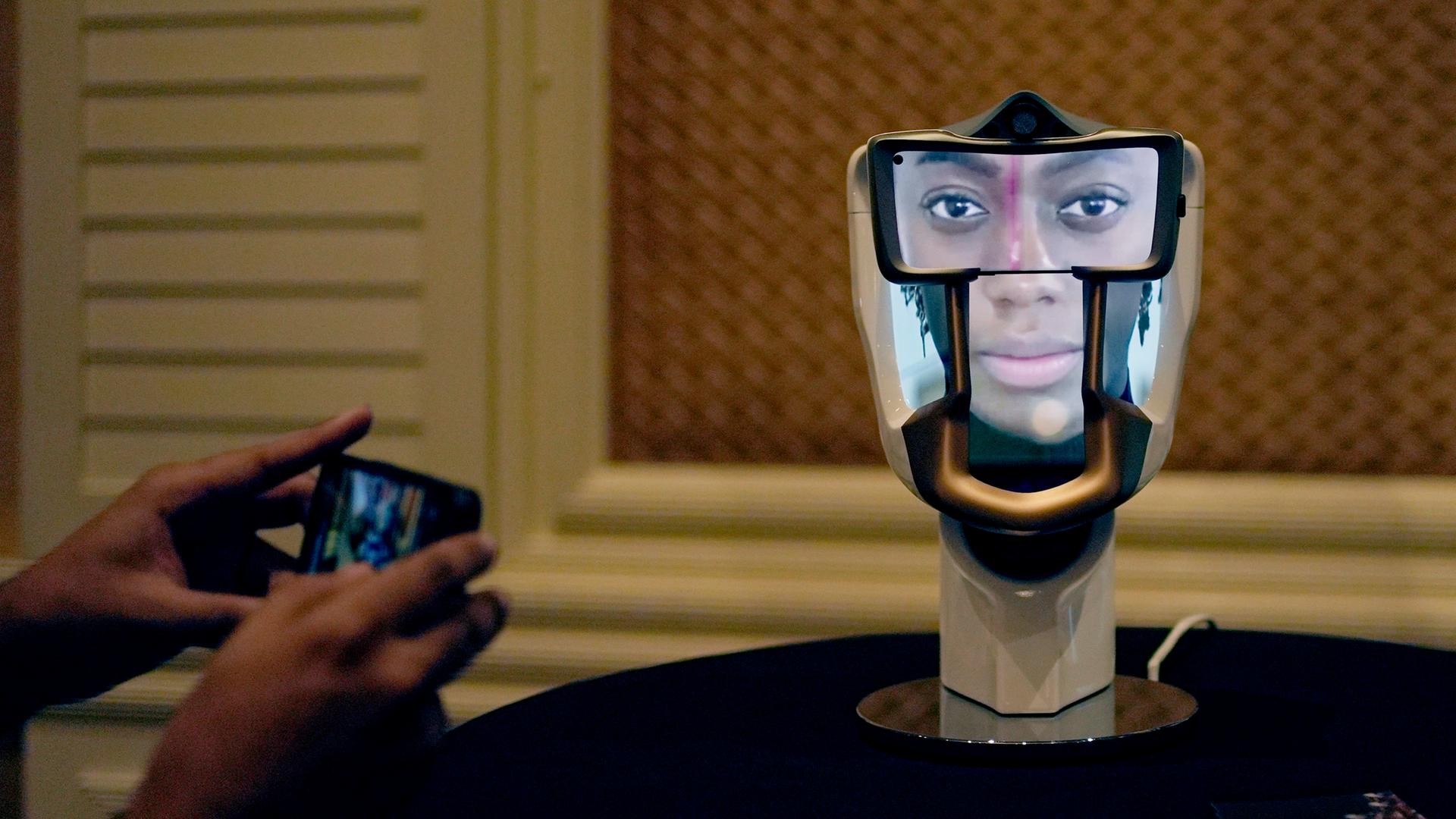 Eine Person macht auf der Technikmesse CES in Las Vegas ein Foto von einem interaktiven KI-Interface: ein Gebilde in der Form eines Schädels, auf das ein Gesicht projiziert ist.