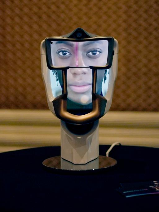 Eine Person macht auf der Technikmesse CES in Las Vegas ein Foto von einem interaktiven KI-Interface: ein Gebilde in der Form eines Schädels, auf das ein Gesicht projiziert ist.