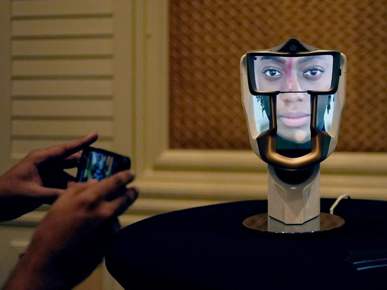 Eine Person macht auf der Technikmesse CES in Las Vegas ein Foto von einem interaktiven KI-Interface: ein Gebilde in der Form eines Schädels, auf das ein Gesicht projiziert ist.
