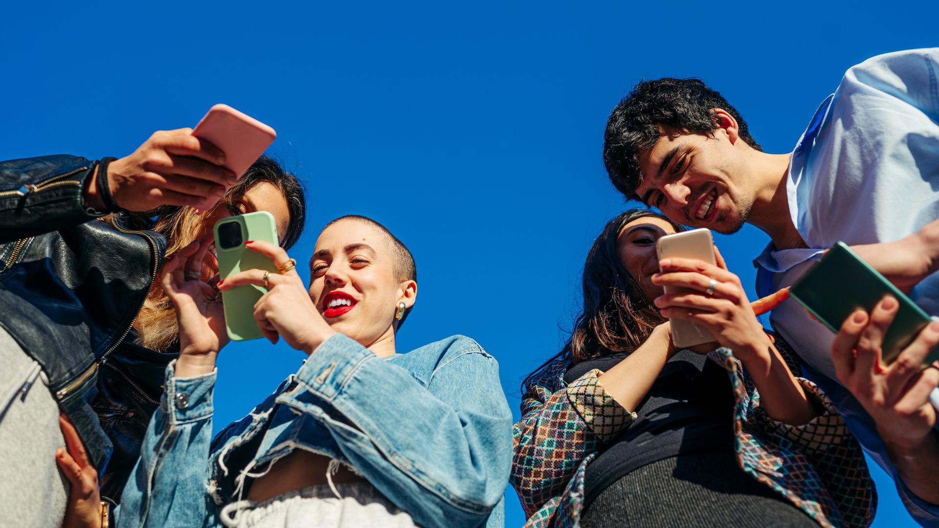 Untersicht auf eine Gruppe von jungen Menschen mit Smartphones.