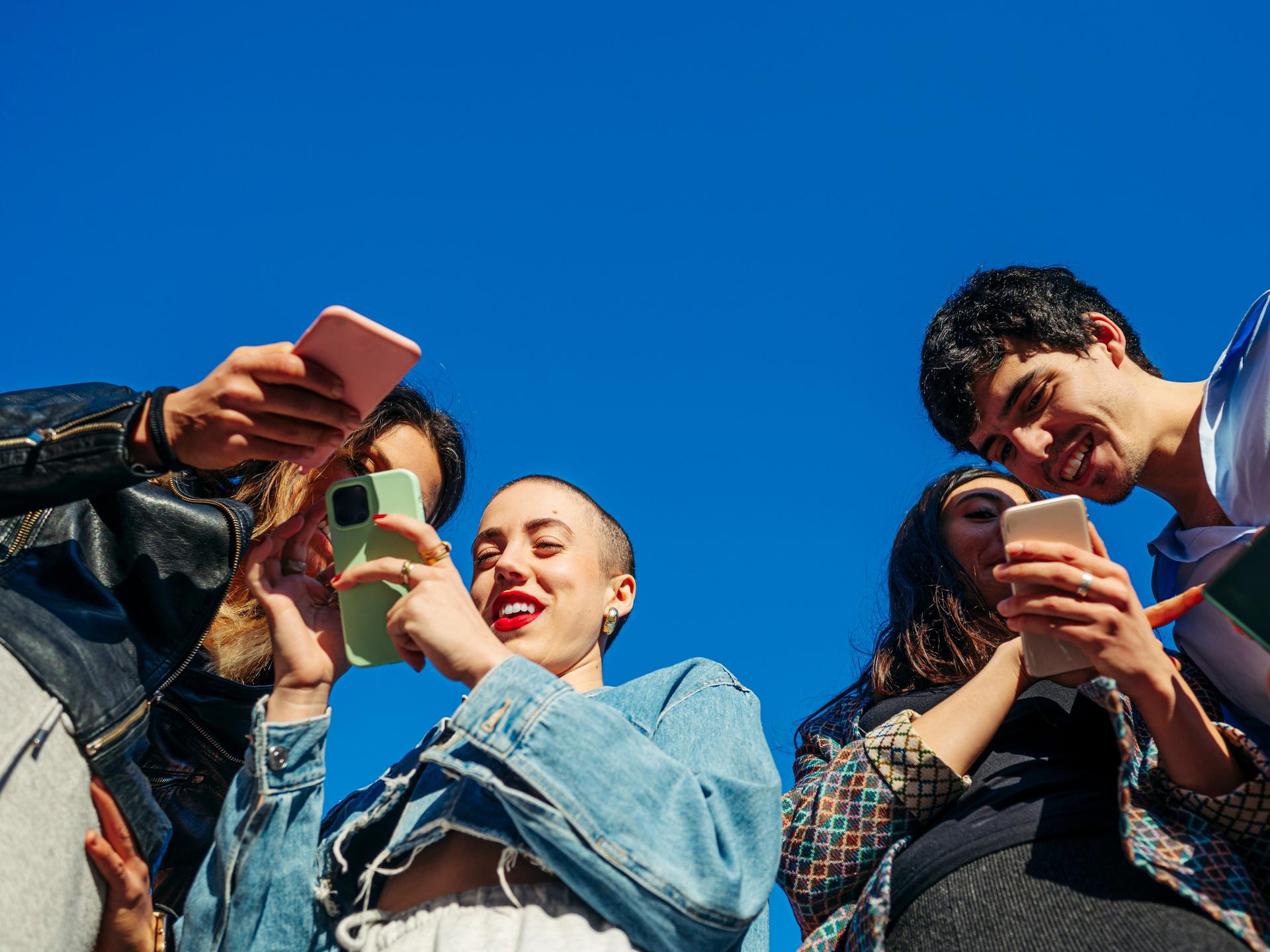 Untersicht auf eine Gruppe von jungen Menschen mit Smartphones.