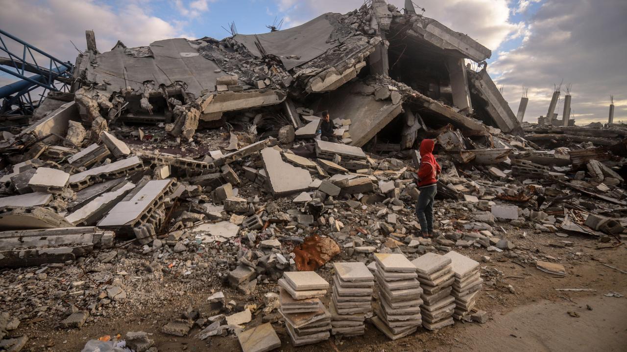 Eine Person mit einem roten Pullover steht vor einem zerstörten Gebäude im Gazastreifen