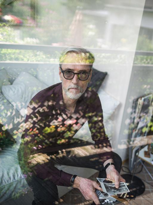 Das Porträt zeigt Peter Keup in seinem Wohnzimmer. In der Hand hält er alte Fotografien.