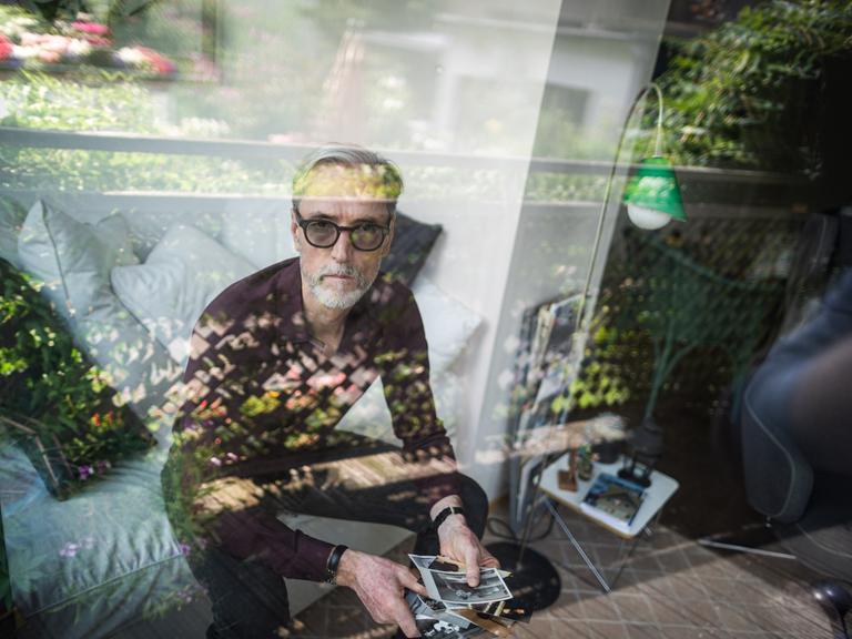 Das Porträt zeigt Peter Keup in seinem Wohnzimmer. In der Hand hält er alte Fotografien.