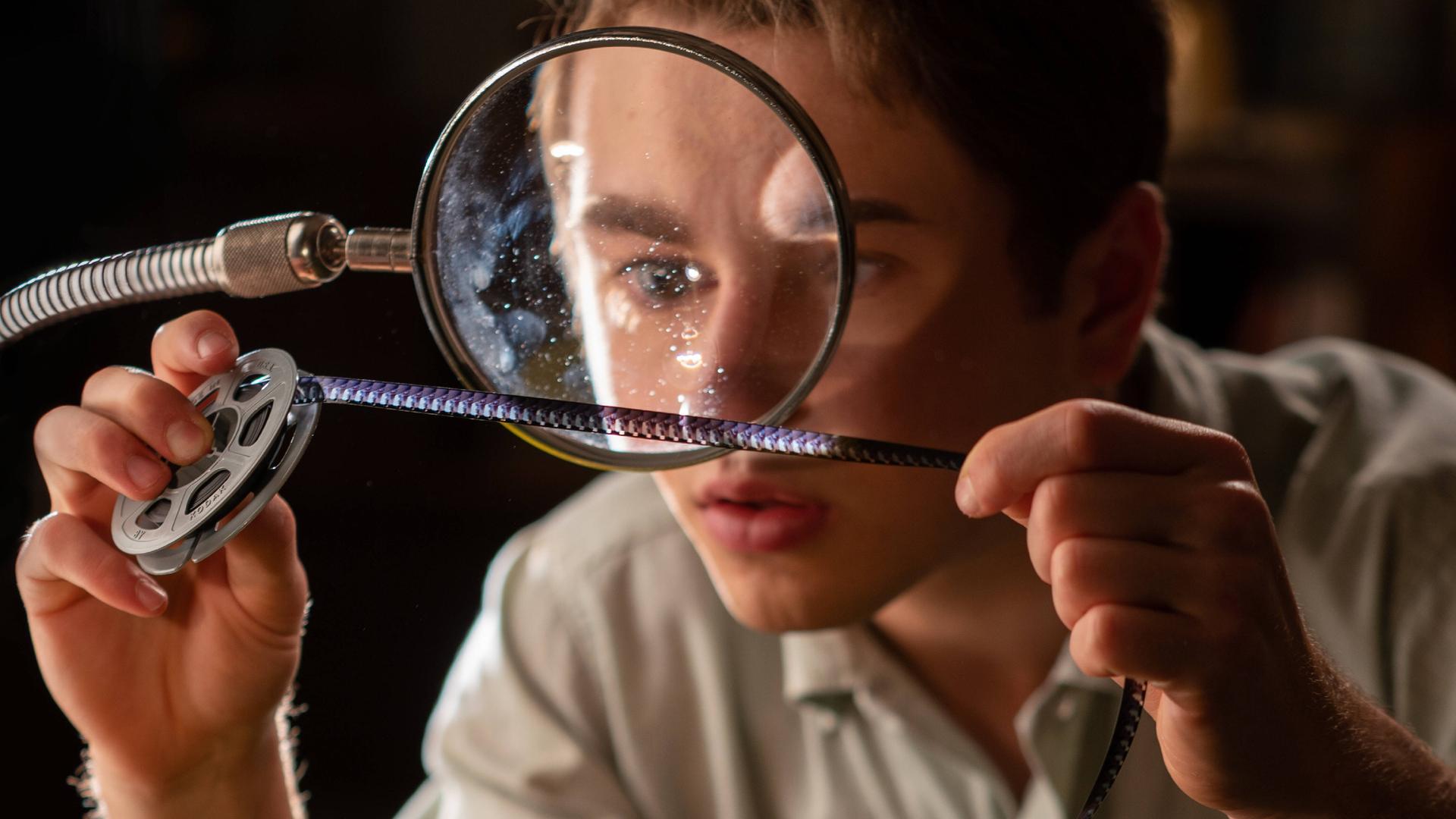 Ein Junge blickt durch ein Vergrößerungsglas staunend auf einen analogen Filmstreifen