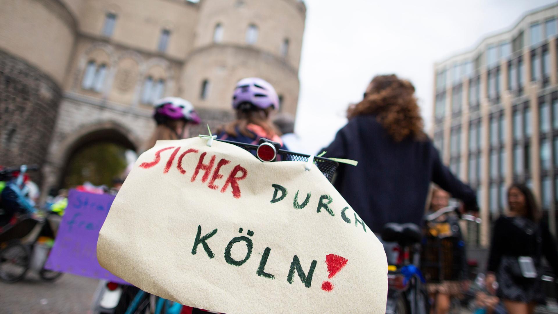 Ein Teilnehmer der bundesweiten Kinderfahrraddemonstration Kidical Mass hat hinten am Fahrrad einen Zettel mit der Aufschrift "Sicher durch Köln".