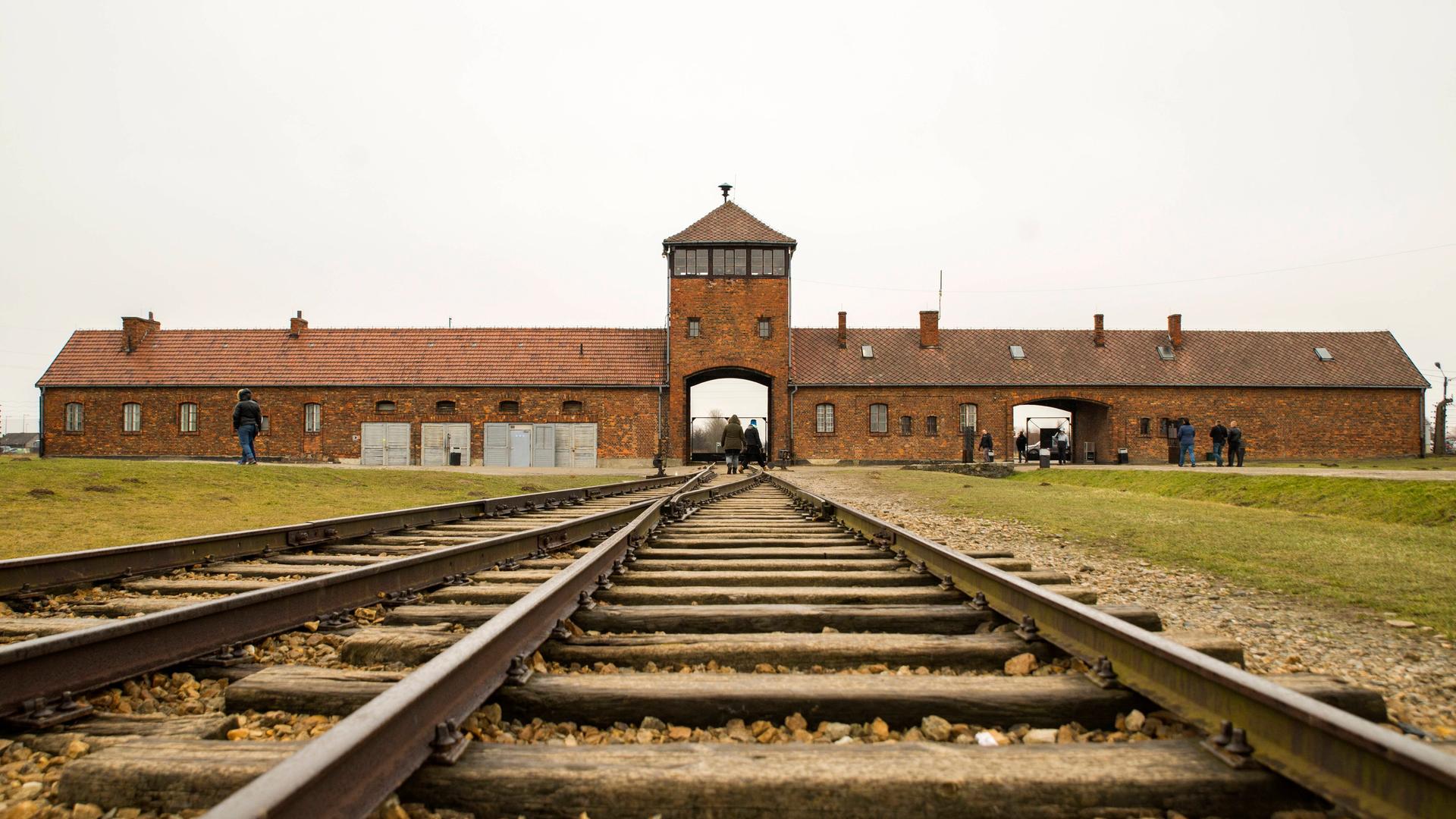 Blick über die Schienen auf das Einfahrttor des KZ Auschwitz, davor stehen Touristen. Blick über die Schienen auf das Einfahrttor des KZ Auschwitz, davor stehen Touristen.