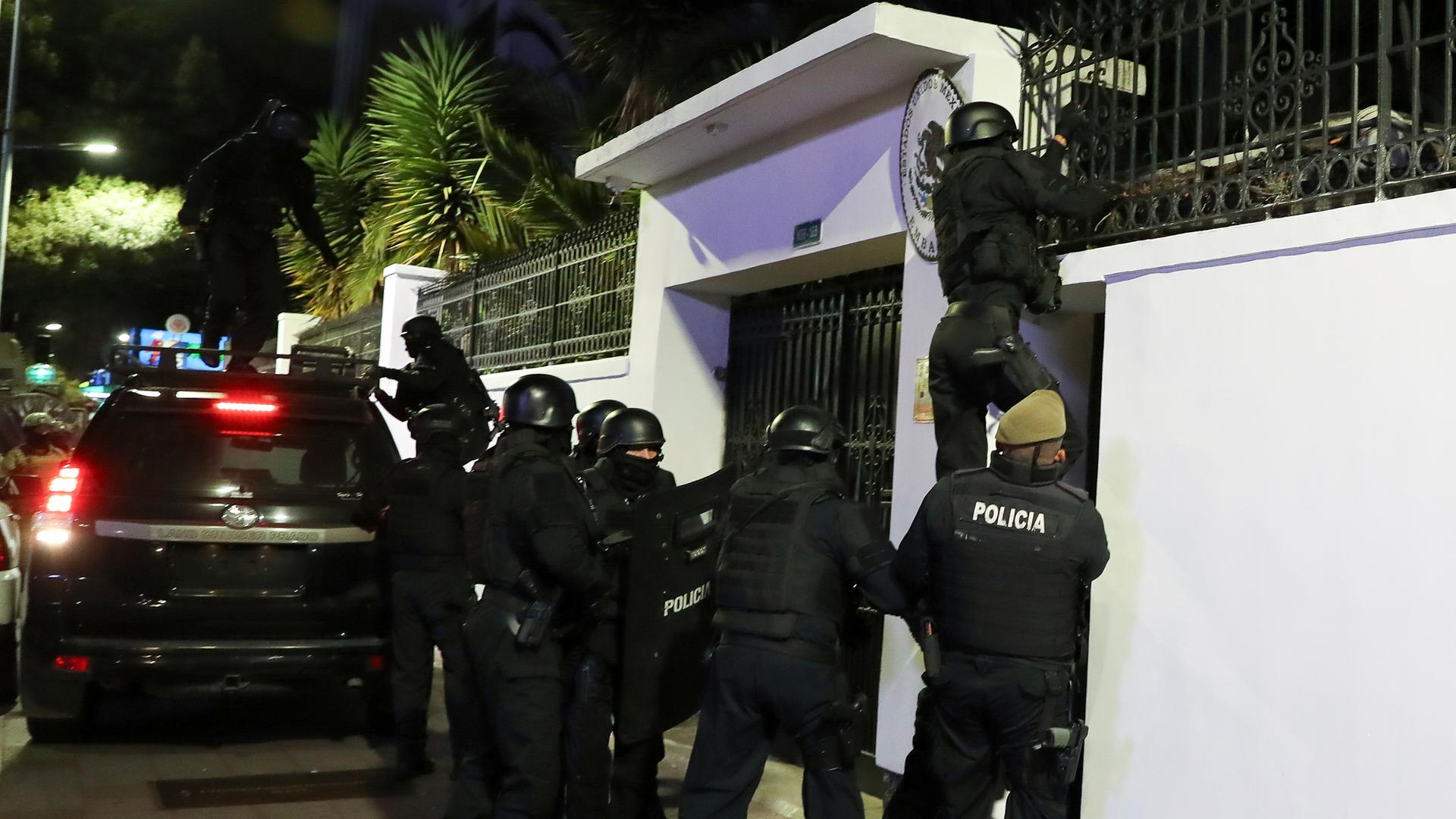 Polizisten in schusssicheren Westen und mit Helmen stehen vor der mexikanischen Botschaft in Quito. Ein Polizist klettert die Mauer hoch.