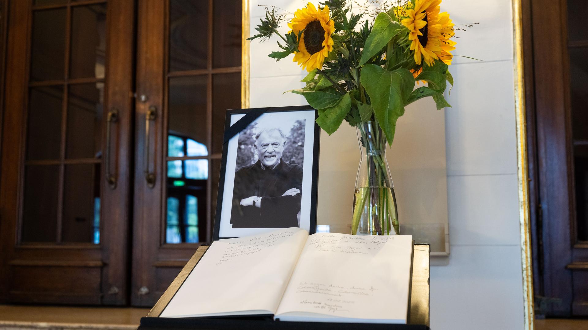 Ein Kondolenzbuch auf einem Tischchen, darauf ein schwarz-umrandetes Foto des Theatermachers Claus Peymann und Sonnenblumen in einer Vase Ein Kondolenzbuch auf einem Tischchen, darauf ein schwarz-umrandetes Foto des Theatermachers Claus Peymann und Sonnenblumen in einer Vase